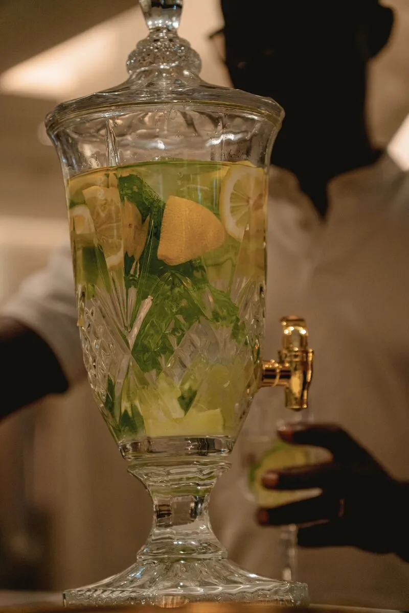 Mão a servir água aromatizada de um dispensador de cristal